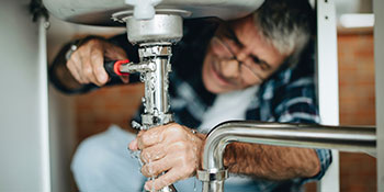 Rental Property Maintenance: Image of man working with a wrench on the pipes beneath a sink.